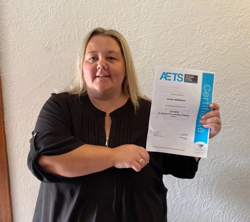 AETS Certificate III in Individual Support (Ageing) graduate, Crisitie smiling while  holding up her AETS graduation certificate 